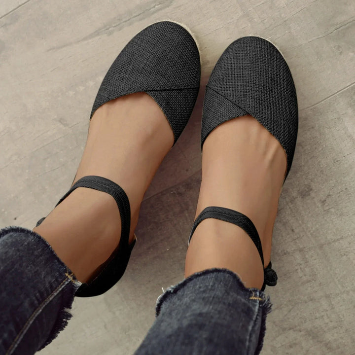 Schwarze Espadrilles mit Knöchelriemen, getragen von einer Person in Jeans. Modische Sommerschuhe, ideal für lässige Outfits und bequemen Stil.