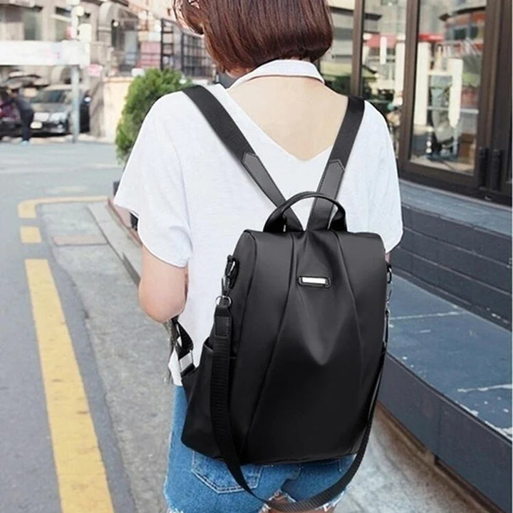 Frau mit schwarzem Rucksack auf einer Stadtstraße, trägt weißes T-Shirt und Jeans. Moderner, stilvoller Rucksack, ideal für den täglichen Gebrauch.