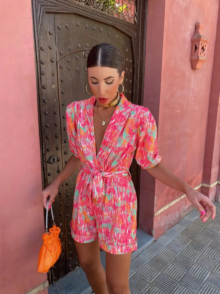 Frau in buntem Sommerkleid vor rosa Wand, hält orangefarbene Tasche. Modetrend, Sommermode, stilvolles Outfit, Stadtbummel.