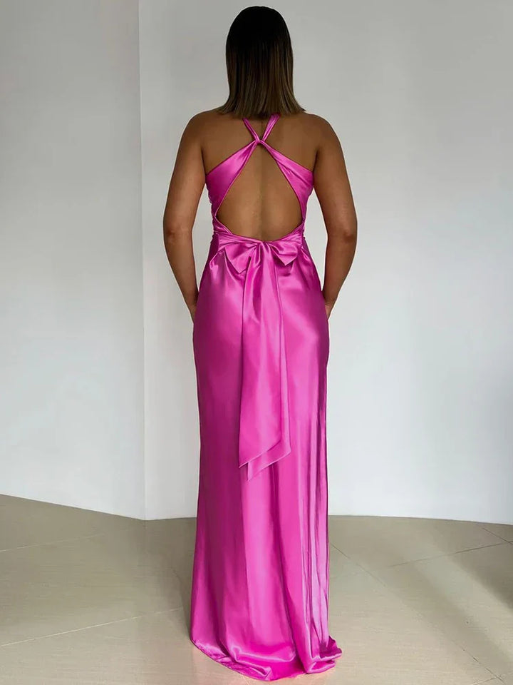 Frau in einem eleganten, rückenfreien, pinken Abendkleid aus Satin mit Schleifendetail, steht vor weißem Hintergrund. Perfekt für formelle Anlässe.
