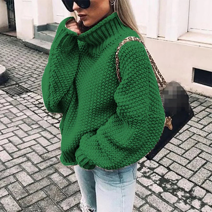 Frau mit grünem Strickpullover und Sonnenbrille, trägt schwarze Tasche, steht auf gepflasterter Straße. Modetrend, Herbstmode, Streetstyle.