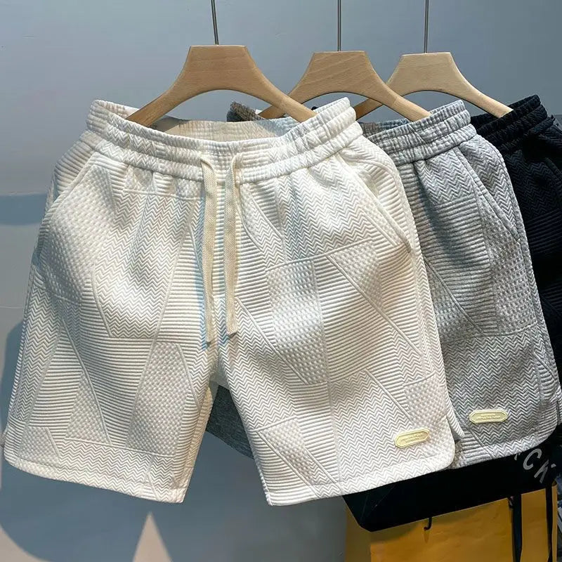 Drei Herren-Shorts auf Kleiderbügeln, in Weiß, Grau und Schwarz, mit geometrischem Muster. Bequeme Freizeitmode, ideal für Sommer und Sport.