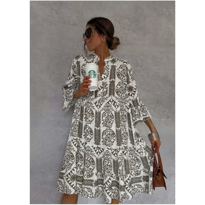 Frau in geblümtem Kleid mit Starbucks-Becher und brauner Handtasche vor grauem Hintergrund. Sommermode, Kaffeegenuss, lässiger Stil.