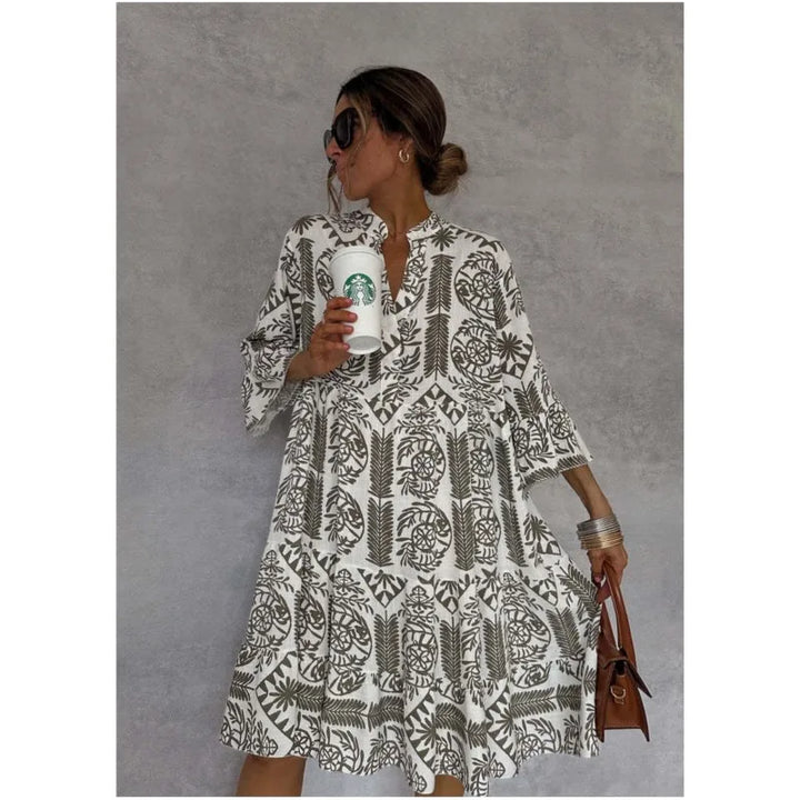 Frau in geblümtem Kleid mit Starbucks-Becher und brauner Handtasche vor grauem Hintergrund. Sommermode, Kaffeegenuss, lässiger Stil.