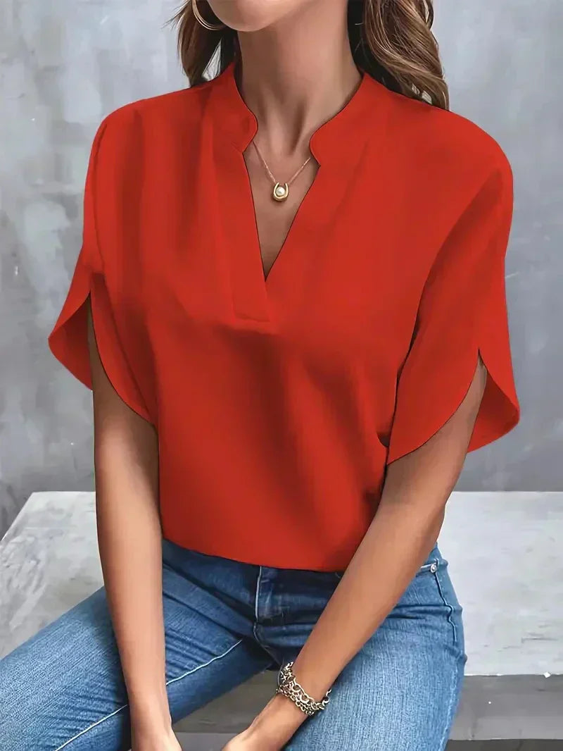 Frau in roter Bluse und blauer Jeans sitzt vor grauem Hintergrund. Modetrend, Damenmode, elegantes Outfit, Freizeitlook.