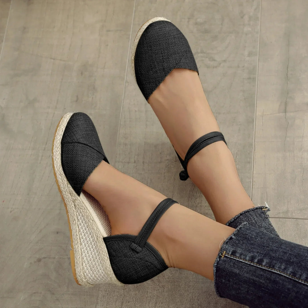 Schwarze Espadrilles mit Keilabsatz und Knöchelriemen auf Holzboden, Damenmode, Sommerschuhe, lässiger Stil, bequemes Design.