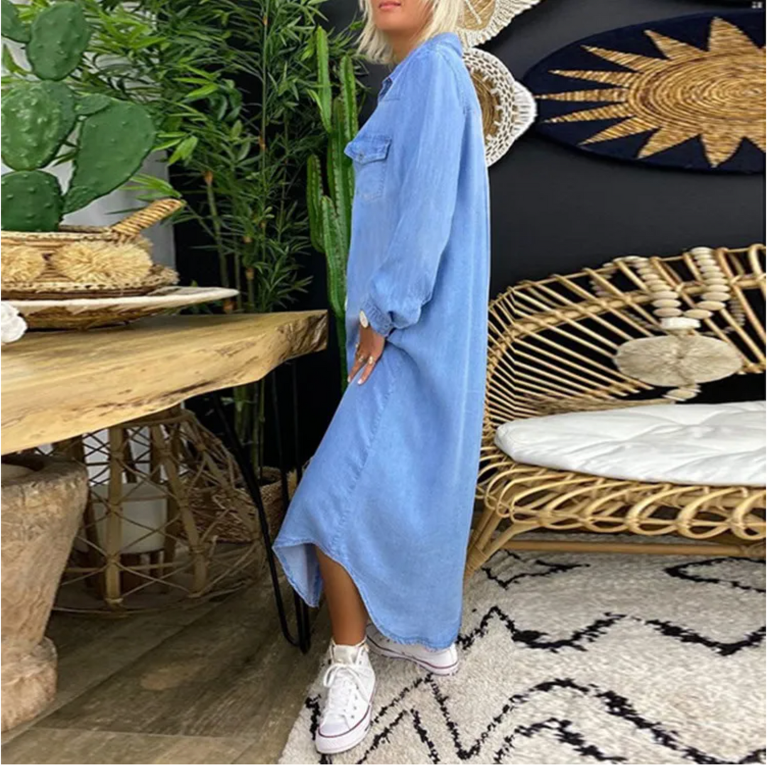 Frau in blauem Maxikleid und weißen Sneakers in modernem Wohnzimmer mit Rattanmöbeln und Pflanzen. Boho-Dekor, stilvolle Inneneinrichtung.