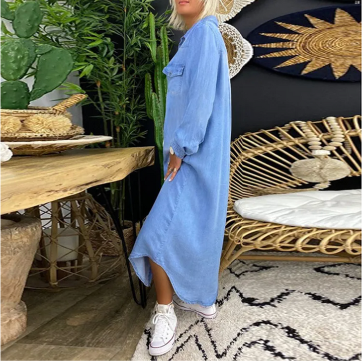 Frau in blauem Maxikleid und weißen Sneakers in modernem Wohnzimmer mit Rattanmöbeln und Pflanzen. Boho-Dekor, stilvolle Inneneinrichtung.