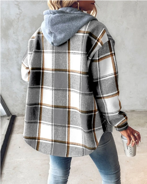 Frau in kariertem Oversize-Hemd mit Kapuze, hält Kaffeebecher. Modetrend Herbst, lässiger Streetstyle, graue Jeans. Rückansicht, urbaner Hintergrund.