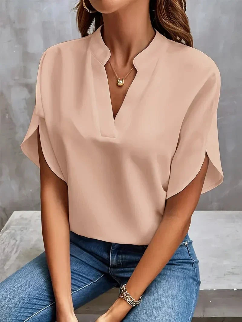 Frau trägt elegante beige Bluse mit V-Ausschnitt und kurzen Ärmeln, kombiniert mit blauen Jeans. Modetrend, Damenmode, stilvolle Freizeitkleidung.