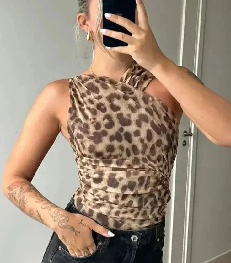 Frau in einem ärmellosen, schulterfreien Leoparden-Top, hält ein Smartphone, trägt schwarze Jeans. Trendige Mode, Tattoo, Selfie.