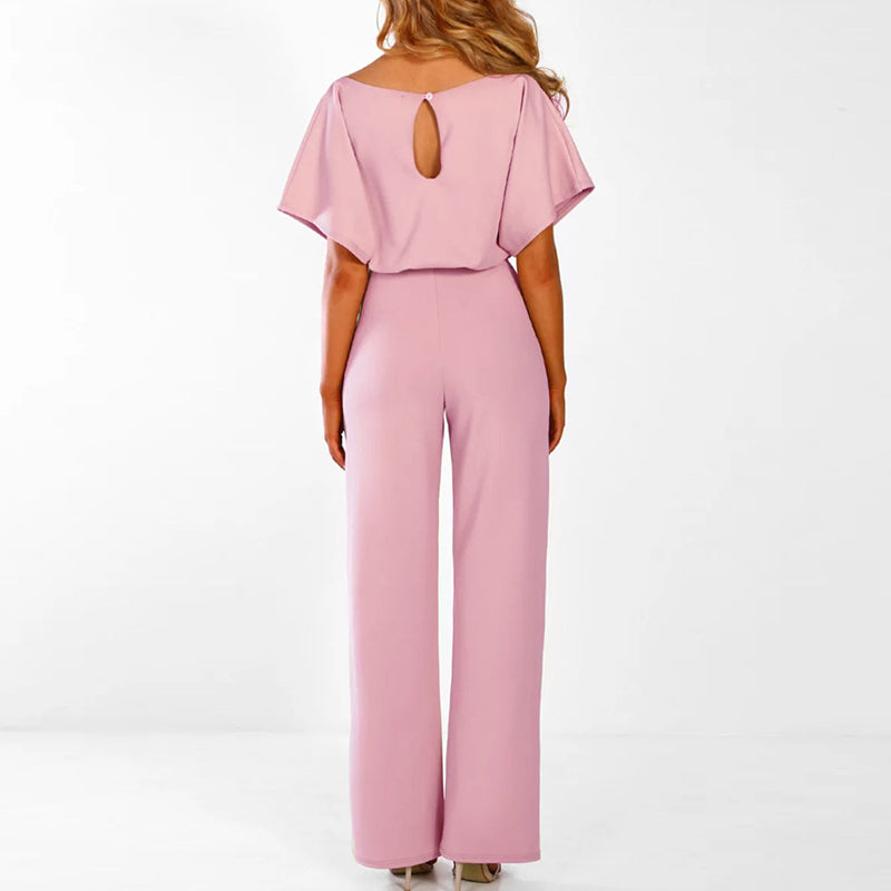 Frau in rosa Jumpsuit mit weitem Bein und kurzen Ärmeln, Rückenausschnitt, stehend vor weißem Hintergrund. Elegante Damenmode, Sommeroutfit.