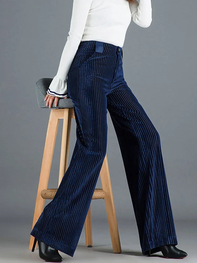 Frau in blauer Cordhose und weißem Oberteil sitzt auf einem Hocker. Modetrend, Damenmode, Cordhose, Herbstmode, stilvoll, elegant.