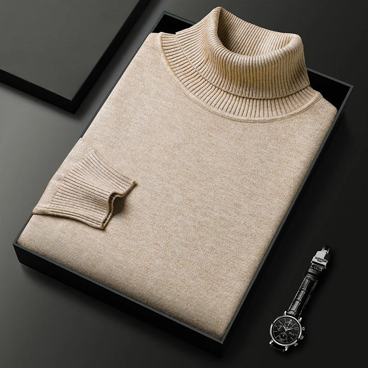 Beigefarbener Rollkragenpullover aus Wolle, elegant gefaltet in schwarzer Box, neben einer stilvollen Armbanduhr auf schwarzem Hintergrund.