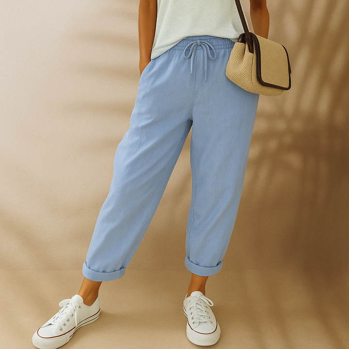 Frau in hellblauer Leinenhose, weißem T-Shirt und weißen Sneakers, trägt eine beige Umhängetasche. Modetrend, lässiger Sommerlook, Damenmode.