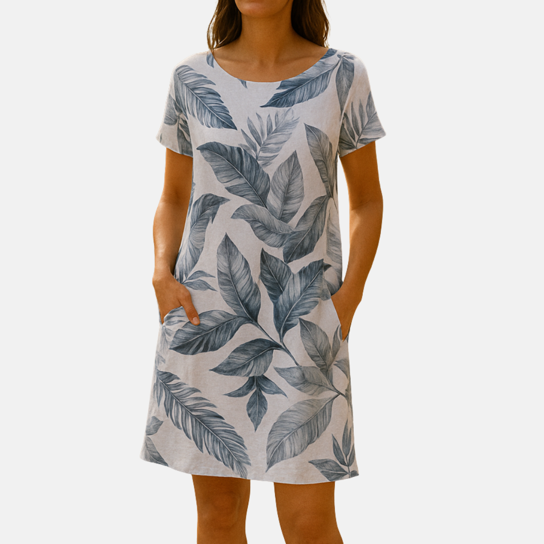 Frau trägt ein sommerliches, knielanges Kleid mit blauen Blättermuster, kurzen Ärmeln und Taschen. Perfekt für Freizeit und Strandmode.