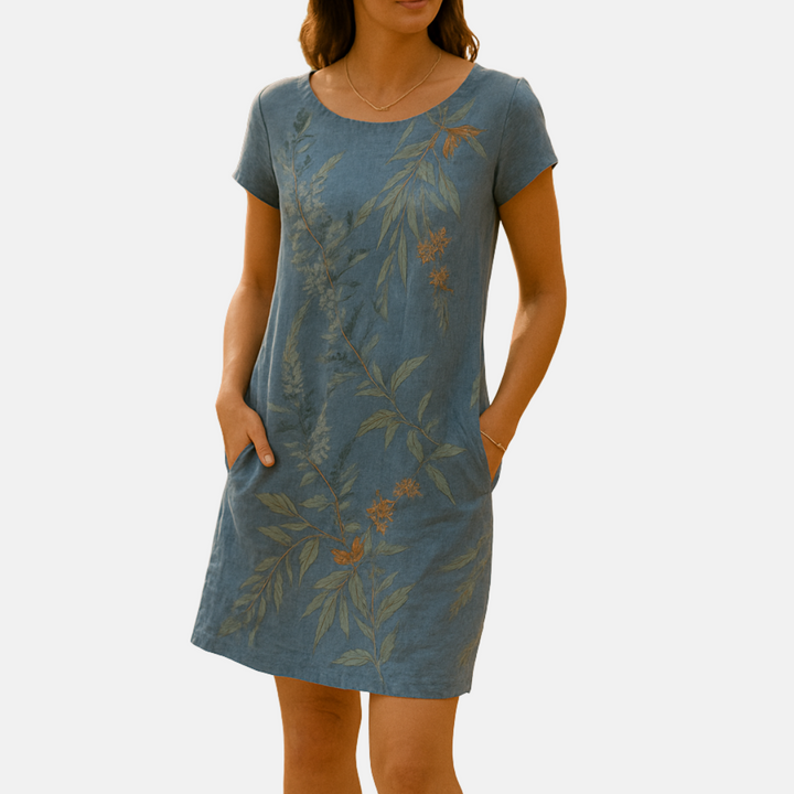 Frau in blauem Leinenkleid mit floralen Mustern, kurzen Ärmeln und Taschen. Sommermode, nachhaltige Kleidung, elegantes Design.
