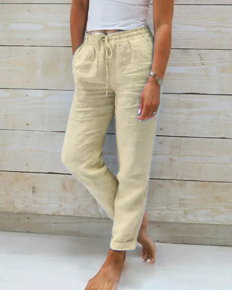 Frau trägt beige Leinenhose mit Kordelzug, kombiniert mit weißem Top. Lässige Sommermode, ideal für Freizeit und Strand.