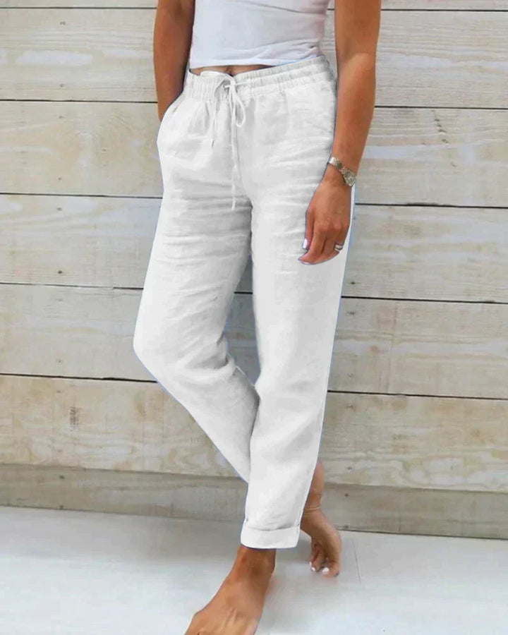 Weiße Leinenhose Damen, lässig, mit Kordelzug, Taschen, bequem, ideal für Sommermode, Freizeitlook, vor hellem Holzhintergrund.