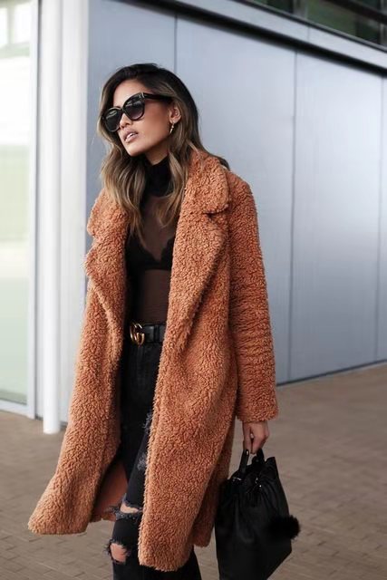 Frau in braunem Teddy-Mantel, schwarze Sonnenbrille, zerrissene Jeans, schwarze Tasche. Modetrend Herbst/Winter, stilvoller Streetstyle-Look.