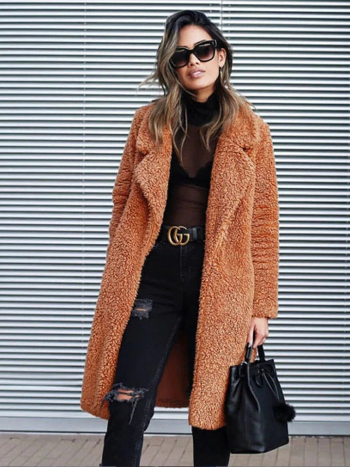 Frau in braunem Teddy-Mantel, schwarze Sonnenbrille, zerrissene Jeans, schwarze Handtasche, vor gestreifter Wand. Modetrend Herbst/Winter.