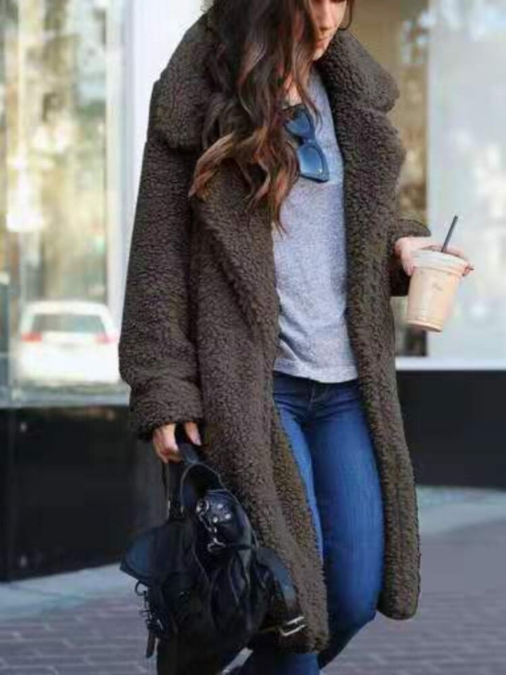 Frau in braunem Teddy-Mantel, grauem Pullover und blauer Jeans, hält Eiskaffee und schwarze Tasche. Wintermode, Straßenstil, lässiger Look.