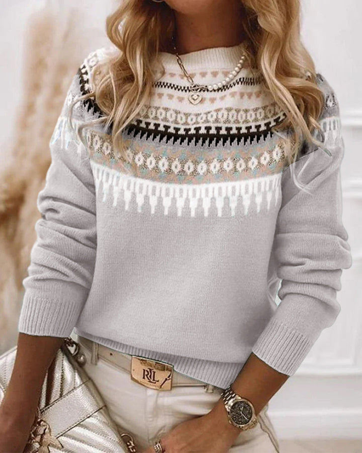 Frau in stilvollem Strickpullover mit Norwegermuster, goldener Halskette und Armbanduhr, hält eine glänzende Handtasche. Elegante Wintermode.