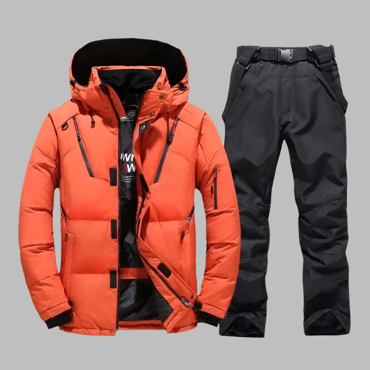 Orangefarbene Winterjacke mit Kapuze und schwarze Skihose auf grauem Hintergrund. Outdoor-Bekleidung, warm, wasserdicht, modisch.