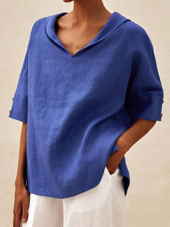 Frau trägt blaues Leinenhemd mit V-Ausschnitt und halblangen Ärmeln, kombiniert mit weißen Hosen. Elegante, lässige Damenmode.