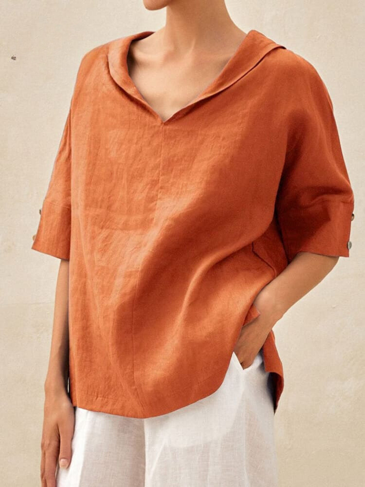 Frau trägt lockere, orangefarbene Leinenbluse mit V-Ausschnitt und weißen Hosen. Modetrend, Sommeroutfit, lässiger Stil, Damenmode.