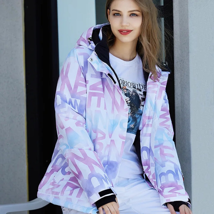 Junge Frau in bunter Winterjacke mit Buchstabenmuster, lächelt vor modernem Gebäude. Modetrend, Wintermode, Damenjacke, stilvoll, urban.
