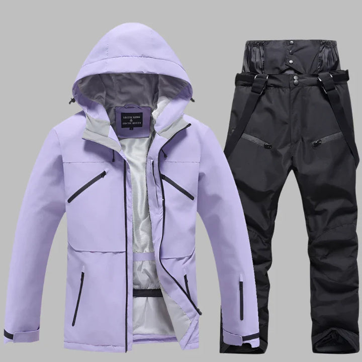 Lila Skijacke mit Kapuze und schwarze Skihose mit Hosenträgern auf grauem Hintergrund. Winterbekleidung, Outdoor, wasserdicht, atmungsaktiv.
