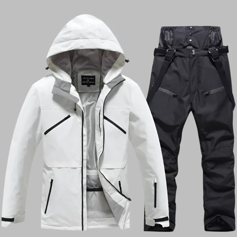 Weiße Skijacke mit Kapuze und schwarze Skihose mit Hosenträgern auf grauem Hintergrund. Winterbekleidung, Outdoor, wasserdicht, atmungsaktiv.