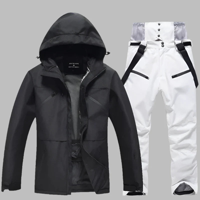 Schwarze Skijacke mit Kapuze und weiße Skihose mit Hosenträgern auf grauem Hintergrund. Winterbekleidung, Outdoor, wasserdicht, atmungsaktiv.