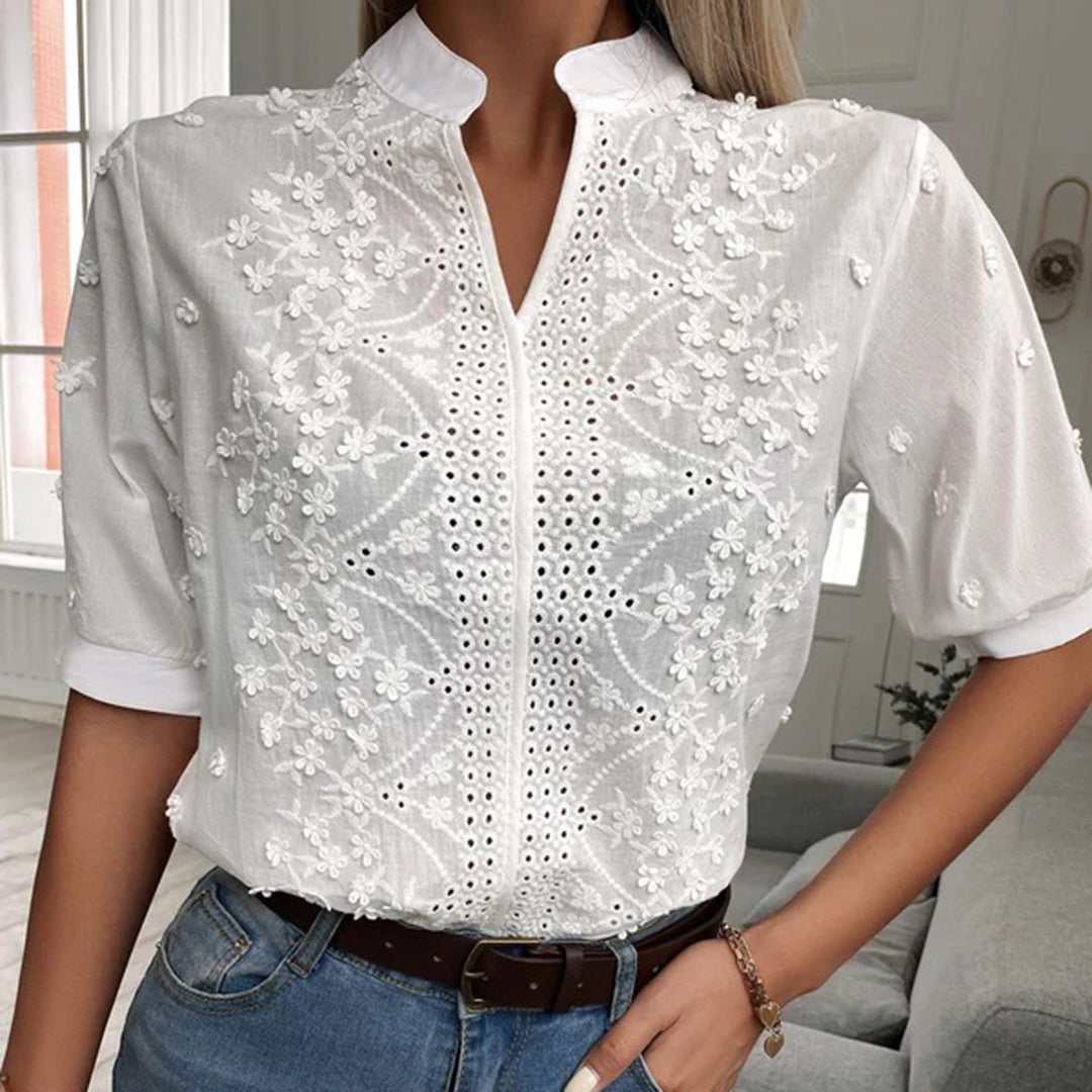 Weiße Damenbluse mit floraler Stickerei und Lochmuster, kombiniert mit blauer Jeans. Elegante Mode für Frühling und Sommer.