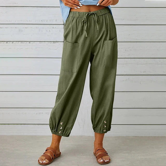 Frau trägt grüne Leinenhose mit Taschen und Knöpfen, kombiniert mit Sandalen. Modetrend, bequeme Damenbekleidung, lässiger Sommerstil.