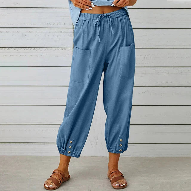 Damenhose in Blau mit elastischem Bund, großen Taschen und Knopfdetails am Saum, kombiniert mit Sandalen. Ideal für lässige Sommermode.