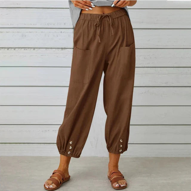Braune Damenhose mit elastischem Bund und Knöpfen an den Knöcheln, kombiniert mit Sandalen. Perfekt für lässige Sommermode und Komfort.