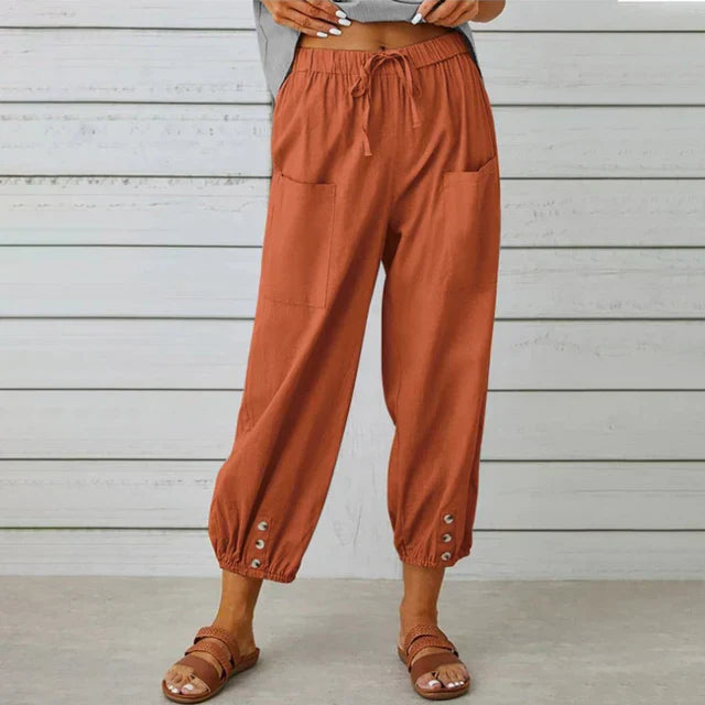 Braune Damen-Leinenhose mit Taschen und Knöpfen am Saum, kombiniert mit Sandalen. Bequeme Sommermode, lässiger Stil, ideal für warme Tage.