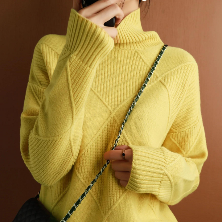 Frau in gelbem Strickpullover mit Rautenmuster, hält Smartphone, schwarze Umhängetasche mit Kettengurt. Modetrend Herbst/Winter 2023.