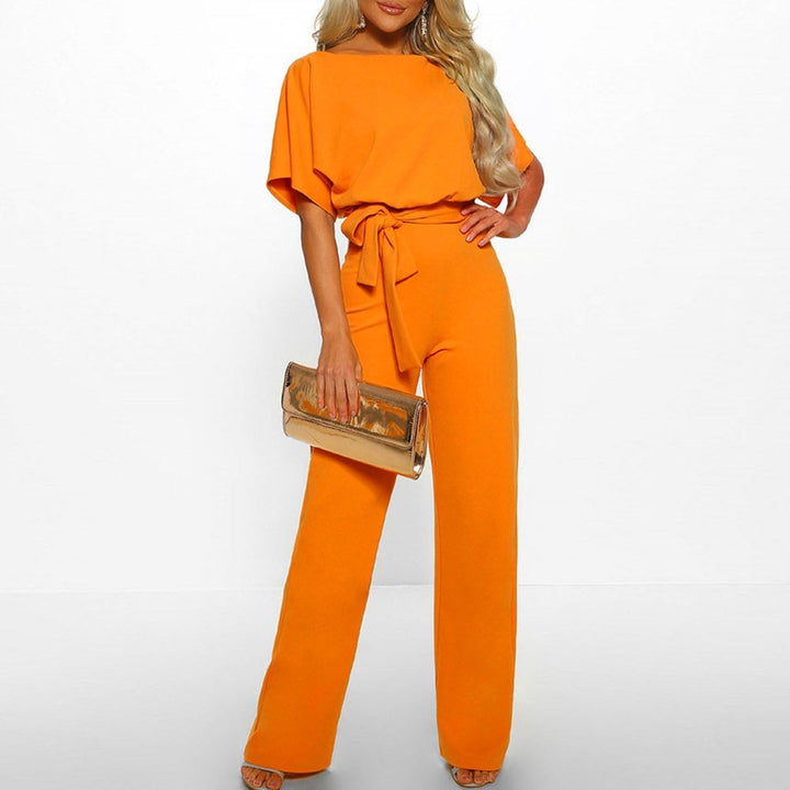 Frau in orangefarbenem Jumpsuit mit Gürtel, hält goldene Clutch. Elegante Mode, stilvolles Outfit, Abendgarderobe, Damenbekleidung.