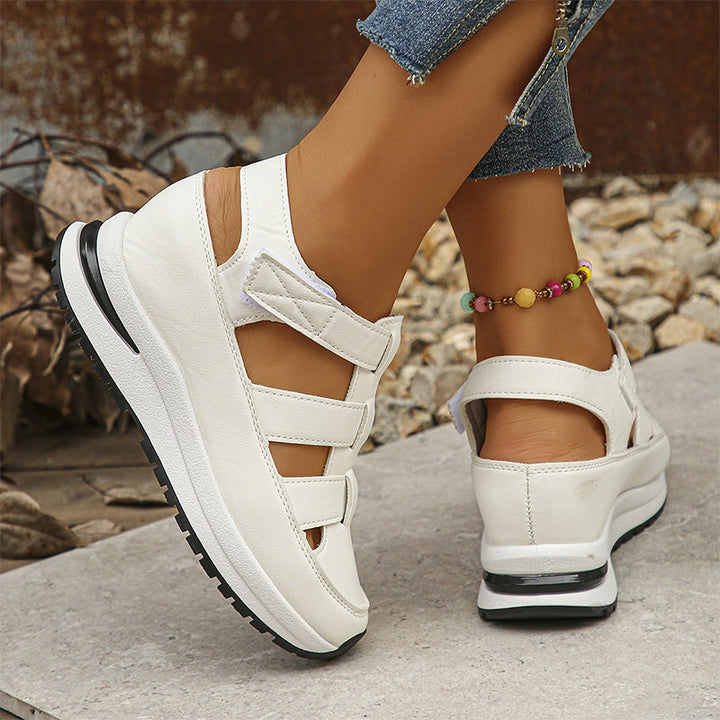 Weiße Damen-Sandalen mit Keilabsatz und Klettverschluss, getragen mit Jeans und bunter Fußkette. Bequeme Sommerschuhe für Damen.