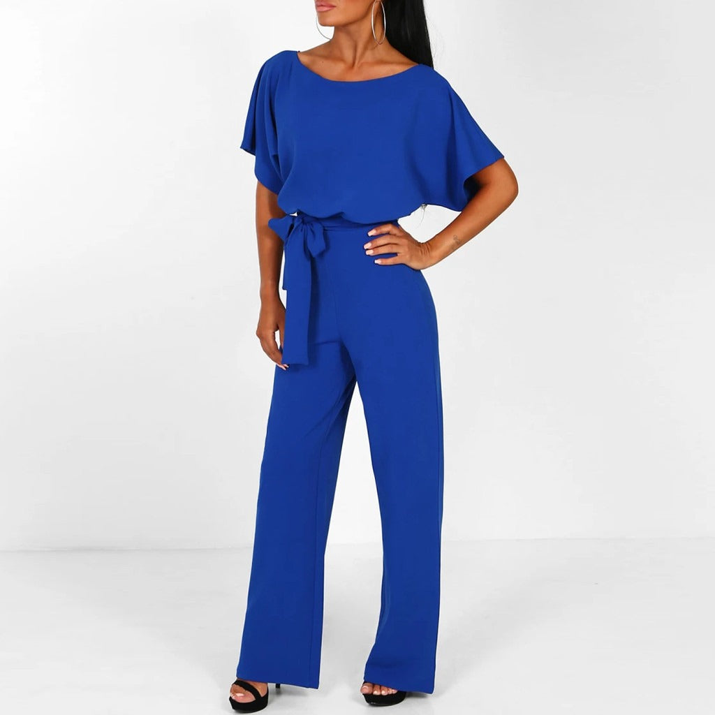 Frau in blauem Jumpsuit mit Gürtel, weiten Ärmeln und schwarzen High Heels vor weißem Hintergrund. Elegante Damenmode, stilvoller Einteiler.