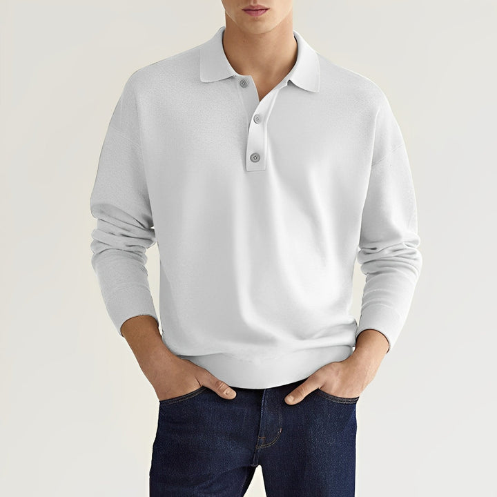 Junger Mann in weißem Poloshirt und blauer Jeans vor neutralem Hintergrund. Modetrend, Herrenbekleidung, lässiger Stil, elegantes Outfit.