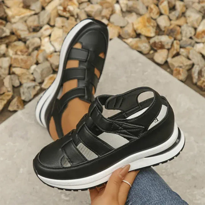Schwarze Damen-Sandalen mit Plateau, sportlich und modern, auf grauem Boden mit Kieselsteinen im Hintergrund. Ideal für Sommermode und Freizeit.