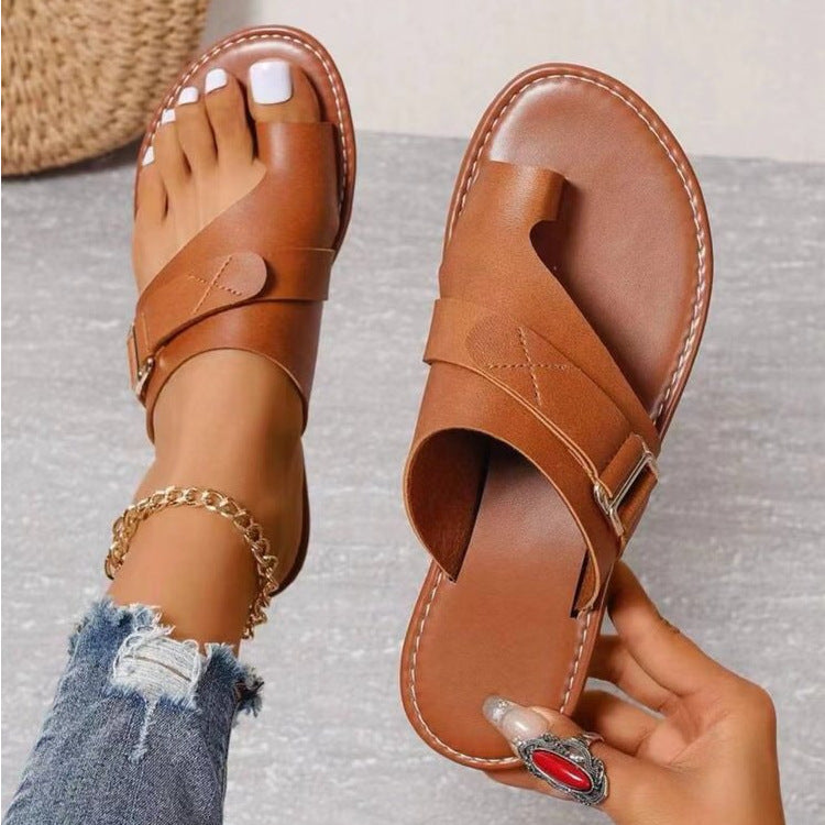 Braune Ledersandalen mit Zehenschlaufe, getragen von einer Person mit Jeans und Fußkettchen. Modische Sommerschuhe, ideal für Damen.