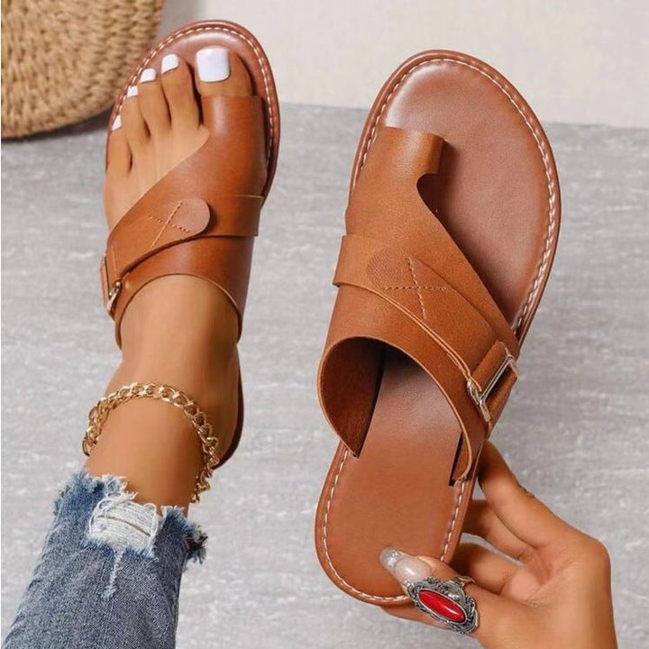 Braune Ledersandalen mit Zehenschlaufe, getragen von einer Person mit Jeans und Fußkettchen. Modische Sommerschuhe, ideal für Damen.