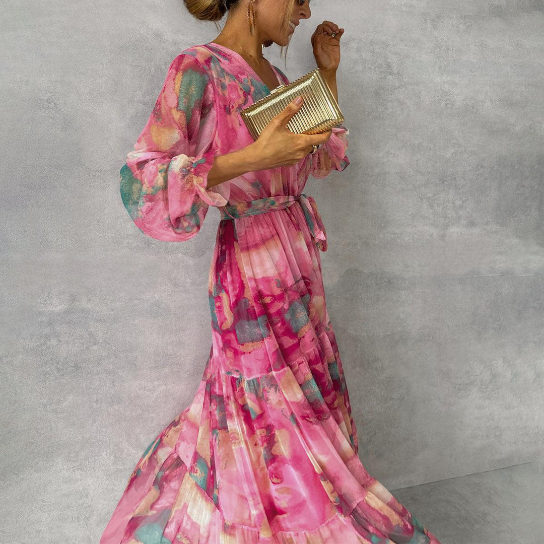 Frau in einem eleganten, pinken Blumenkleid mit langen Ärmeln, hält eine goldene Clutch. Perfekt für Abendmode und stilvolle Anlässe.