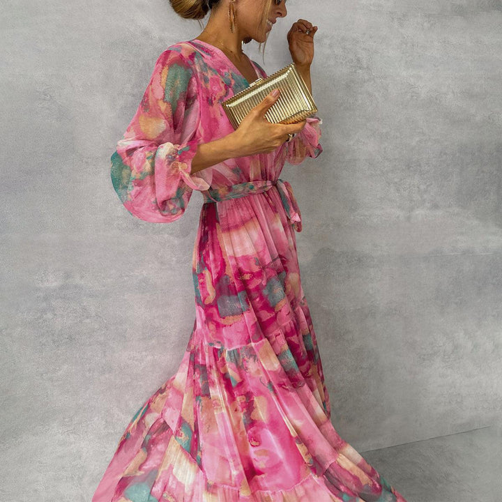 Frau in einem eleganten, pinken Blumenkleid mit langen Ärmeln, hält eine goldene Clutch. Perfekt für Abendmode und stilvolle Anlässe.