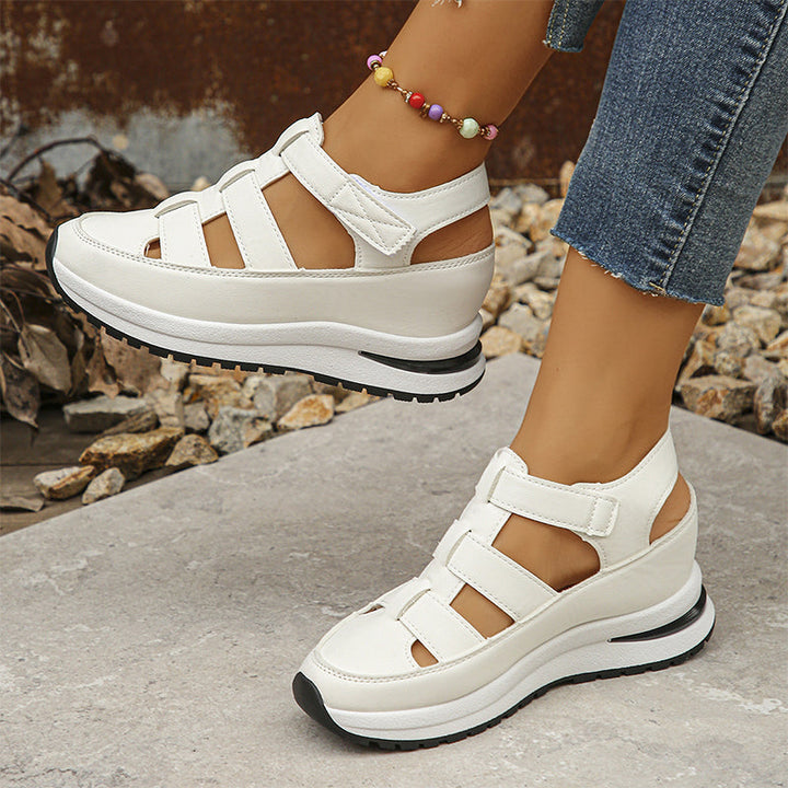 Weiße Plateau-Sandalen mit Klettverschluss an Frauenfüßen, kombiniert mit blauen Jeans. Modische Sommerschuhe, bequem und stilvoll.